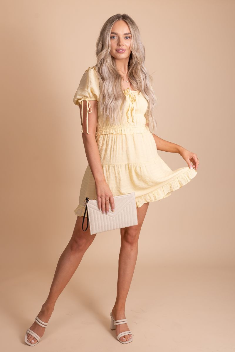 Image of a Prepare For What's Next Mini Dress, featuring a fitted silhouette in pink and yellow. The dress has a square neckline and puffy sleeves. The hemline hits mid-thigh, and the dress appears to be made of stretchy material. The overall look is simple and elegant, with tie embellishments and cinching patterns.