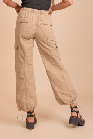 Image of a pair of tan cargo pants on a model in front of tan background. The pants have a relaxed fit with multiple pockets located on the sides of the legs. The fabric appears to be sturdy and textured, with a slightly faded look to it.