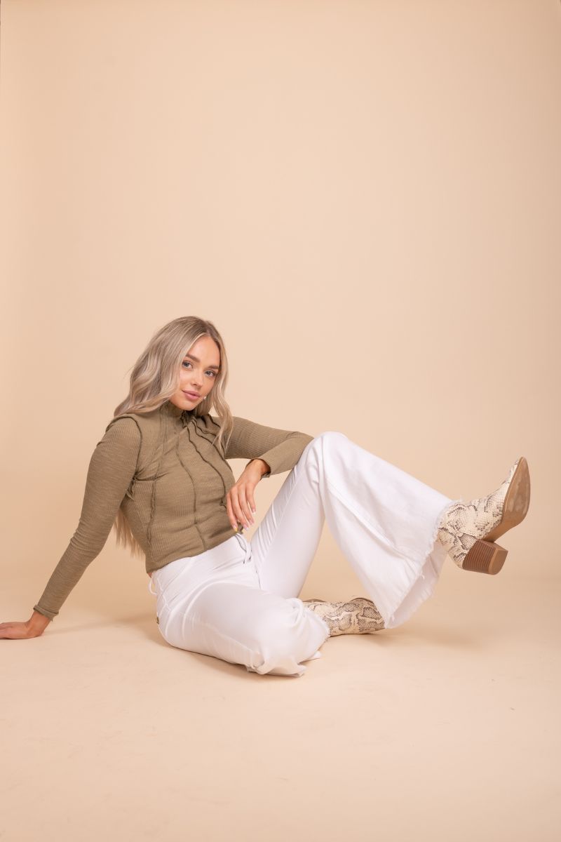 Image of a Full Of Happiness Mock Neck Top from Bella Ella Boutique, featuring black, brown and green color options. The model is wearing them in front of tan background. The top has a high neckline and long sleeves with a ruffled detail at the cuffs. The fabric appears to be lightweight and breathable, with a soft texture.