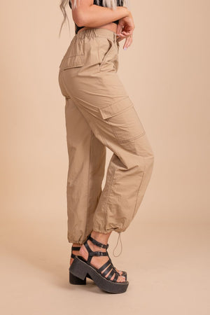 Image of a pair of tan cargo pants on a model in front of tan background. The pants have a relaxed fit with multiple pockets located on the sides of the legs. The fabric appears to be sturdy and textured, with a slightly faded look to it.