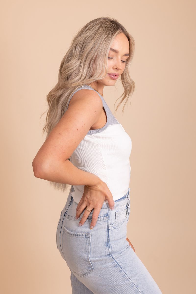 Image of a white and grey color block tank top on a model in front of a tan background. The top has a round neckline with the top half being white and the bottom half being gray alternating. The fabric appears to be a soft and lightweight material with a subtle texture.