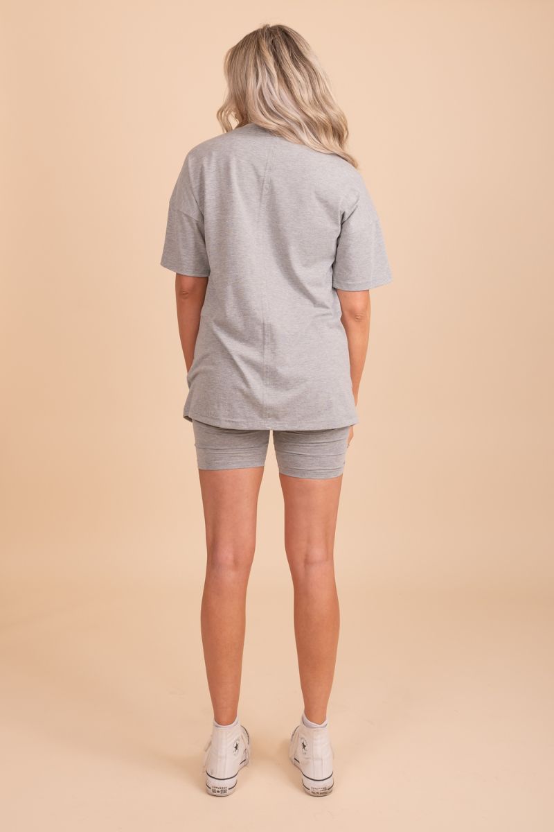 Image of a grey matching set featuring shorts and a short-sleeved top on a model in front of a background. The shorts have a relaxed fit with an elastic waistband and the top has a crew neckline and a loose, comfortable fit. The fabric appears to be lightweight and soft, with a heathered texture and a subtle sheen to it