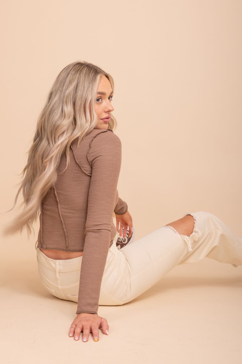 Image of a Full Of Happiness Mock Neck Top from Bella Ella Boutique, featuring black, brown and green color options. The model is wearing them in front of tan background. The top has a high neckline and long sleeves with a ruffled detail at the cuffs. The fabric appears to be lightweight and breathable, with a soft texture.