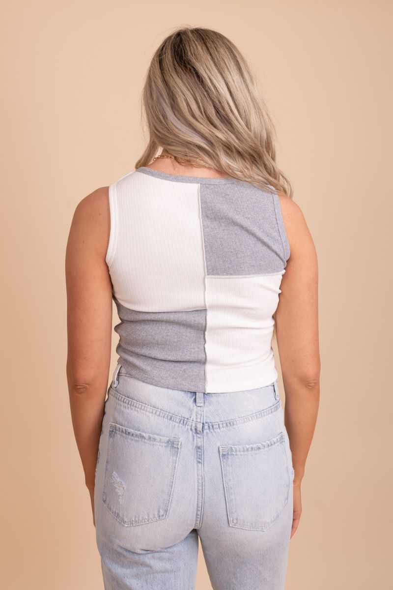 Image of a white and grey color block tank top on a model in front of a tan background. The top has a round neckline with the top half being white and the bottom half being gray alternating. The fabric appears to be a soft and lightweight material with a subtle texture.